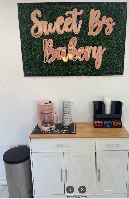 Sweet B's Bakery sign on a hedge wall above the coffee station